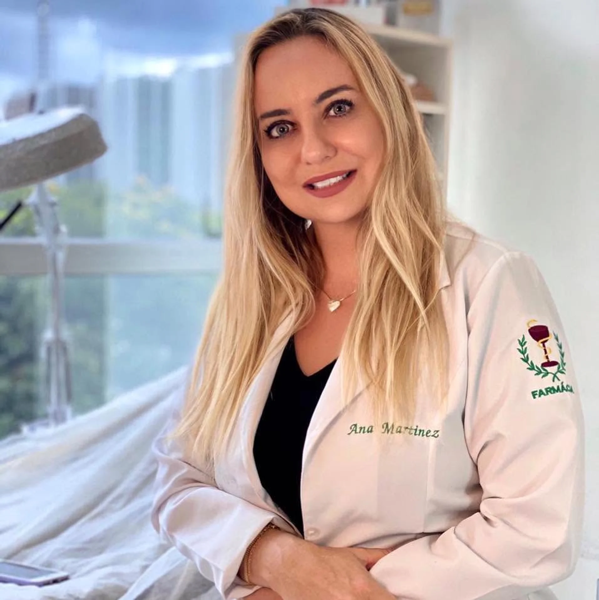 Dra. Ana Martinez de jaleco, sorrindo, na sala de atendimento, com a janela ao fundo