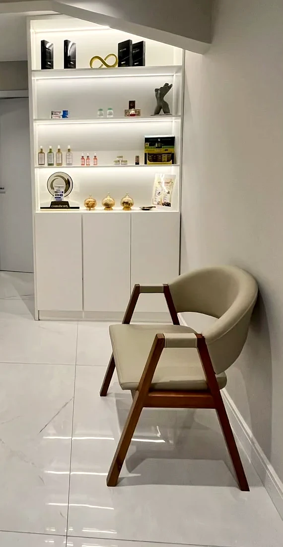 Estante iluminada da recepção, com produtos e um laço dourado na prateleira de cima, e uma poltrona ao lado