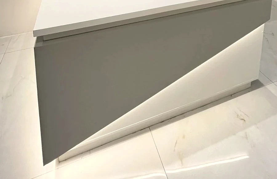 Balcão da recepção: tampo branco, frente cinza cortada em diagonal por uma faixa de luz, sobre o piso de porcelanato branco